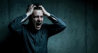 Stressed businessman screaming with hands on head against dark concrete wall showing mental breakdown and workplace pressure.