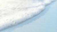 Gentle ocean wave washing onto pristine white sand beach with soft foam and crystal clear turquoise water creating peaceful coastal scene for relaxation concepts.