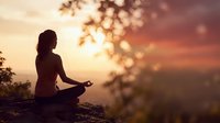 Woman meditating in lotus pose during golden hour sunset with warm bokeh lights and silhouetted trees creating peaceful spiritual atmosphere for wellness content.