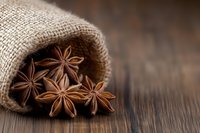 Star anise pods spilling from rustic burlap sack onto dark wooden surface, warm brown tones create cozy autumn mood for culinary and seasonal designs.