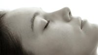 Serene woman with closed eyes in peaceful meditation pose, soft lighting creates calming atmosphere for wellness and mindfulness concepts.