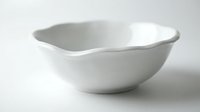 White ceramic bowl with wavy rim isolated on white background for kitchen and dining design projects.