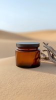 Amber glass cosmetic jar on sandy desert dunes with driftwood, minimalist eco-friendly skincare packaging in natural sunlight, wellness spa concept.