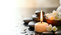 Spa wellness scene with burning candle, hot stones, jasmine flowers in wooden bowl and water droplets creating peaceful relaxation atmosphere.