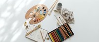Artist workspace with wooden palette, colored pencils, brushes and canvas on white background for creative projects and art education.
