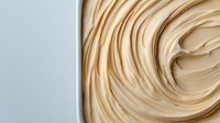 Smooth swirls of creamy beige frosting texture in white container, macro close up view showing soft peaks and glossy surface. For food photography and bakery design.