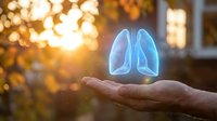 Glowing holographic lungs floating above open palm at sunset representing respiratory health, medical care, and wellness technology concepts.