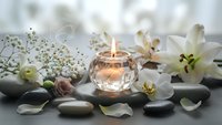 Spa wellness scene with burning candle, white lilies, smooth stones and delicate flowers creating peaceful relaxation atmosphere for meditation and self-care.