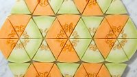 Colorful cantaloupe and honeydew melon slices arranged in a geometric pattern on a white marble surface, top view.