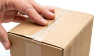 Close-up of hand sealing cardboard shipping box with tape for delivery and logistics purposes.