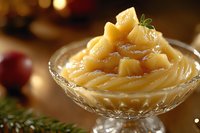 Sweet vanilla pudding topped with caramelized pear chunks served in elegant crystal dessert bowl, garnished with mint leaf against warm festive background.