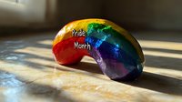 Rainbow colored macaroon cookie on wooden surface in natural sunlight casting soft shadows, symbolizing diversity and celebration of pride community.