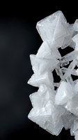 Clear white salt crystals formation on dark background showing natural mineral structure and geometric patterns for scientific education.