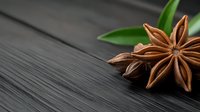 Star anise spice on dark wooden background with green leaves. Aromatic cooking ingredient for culinary recipes and natural seasoning applications.