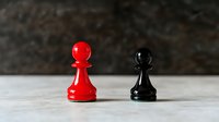 Red and black chess pawns facing each other on light surface against dark background, symbolizing competition, strategy and opposition in business or life.