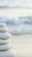 Zen stone stack on peaceful beach with soft ocean waves creating serene meditation and wellness atmosphere for mindfulness and relaxation practices.