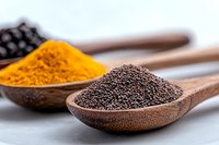 Wooden spoons filled with black pepper and turmeric powder on white background, macro food photography showing texture and detail of aromatic spices.