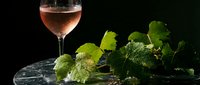 Elegant rose wine glass with fresh grape vine leaves on dark marble surface, perfect for wine tasting, vineyard marketing, and culinary photography projects.