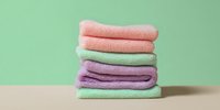 Stack of colorful folded towels in pastel pink, green, and purple on beige surface against mint green background for spa, bathroom, or home decor.