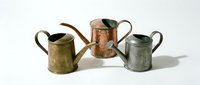 Vintage metal pitchers and jugs in brass, copper, and patina finishes arranged on white background for antique decor and design projects.