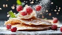 Fresh raspberries and powdered sugar falling onto layered crispy crepes garnished with mint leaves, captured in dynamic motion against dark background.