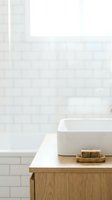 Minimalist bathroom vanity with white ceramic sink, wooden cabinet, and natural soap bar on wooden tray against white subway tile wall with window light for spa and home decor design.