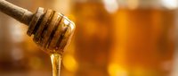 Golden honey dripping from wooden dipper with warm amber background for natural sweetness and organic food concepts in kitchen or culinary applications.