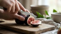 Hand slicing fresh figs on wooden cutting board in kitchen, food preparation and cooking ingredient for culinary use.