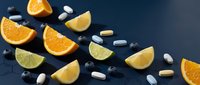 Fresh citrus fruit slices with vitamin supplements on dark background. Healthy nutrition concept with orange, lemon and lime wedges plus pills.