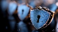 Water droplets on metallic shield-shaped security lock symbol with keyhole, glowing blue cybersecurity concept on dark background with bokeh effect.