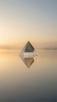 Crystal glass pyramid floating on calm water surface with golden sunset reflection creating serene minimalist composition for meditation and wellness concepts.