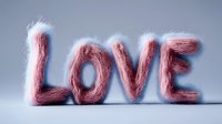 Pink fluffy letters spelling out LOVE against soft blue background, created with wool or fur-like material texture for romantic and Valentine's day designs.