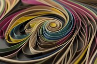 Colorful paper quilling strips forming dynamic spiral patterns with flowing curves in purple, gold, teal and cream tones for creative crafting projects.