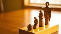 Wooden nativity scene figurines on table with warm sunlight streaming through window creating peaceful Christmas atmosphere for holiday decorations.