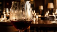 Glass of red wine with condensation droplets in elegant restaurant setting with warm ambient lighting and blurred background creating sophisticated dining atmosphere.