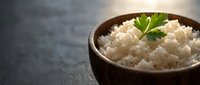 Steamed white rice in wooden bowl garnished with fresh parsley on dark stone surface for healthy meal preparation and Asian cuisine cooking concepts.