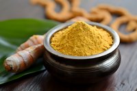 Turmeric powder in traditional bowl with fresh root and green leaf on wooden surface for cooking and natural health remedies.