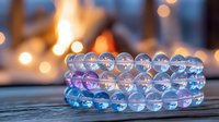 Luminous crystal beaded bracelets in pastel blue and purple colors on wooden surface with soft bokeh lights creating magical atmospheric background.