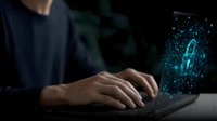 Digital security concept with glowing blue padlock hologram emerging from laptop keyboard while person types, representing cybersecurity and data protection in modern workplace.