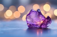 Purple amethyst crystal gemstone on reflective surface with warm bokeh lights background for meditation wellness and spiritual healing practices.