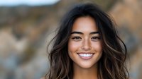 Young Asian woman with natural wavy hair and bright authentic smile outdoors in soft evening light, looking directly at camera with confident expression.