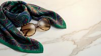 Elegant silk scarf with paisley pattern and vintage sunglasses on marble surface. Luxury fashion accessories for sophisticated style and travel.