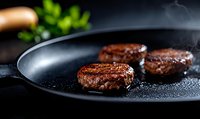 Juicy beef burger patties sizzling on black cast iron pan with rising steam and herbs in background, close-up view showing grilled meat texture and cooking process.