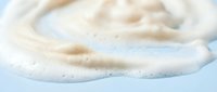 Creamy white foam swirl with soft bubbles on light blue background for skincare cosmetics and beauty product applications.