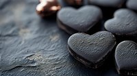 Dark chocolate heart-shaped cookies with cream filling on black stone background, romantic dessert concept for Valentine's Day celebration and sweet treats.