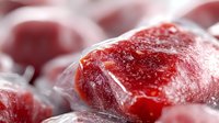 Frozen red meat chunks covered in frost crystals, macro close-up view showing raw texture and crystalline structure. Food preservation concept.