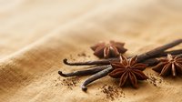 Aromatic star anise and vanilla beans arranged on wooden surface with scattered spice powder for culinary and cooking projects.