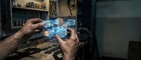 Craftsman hands holding futuristic holographic interface in traditional workshop blending old tools with modern technology for industrial innovation.