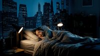 Young woman sleeping peacefully in bed with city skyline view through window at night, urban bedroom interior with warm lighting and modern architecture.