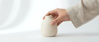 Close-up of a hand touching a smooth, cream-colored ceramic vessel on white surface, suitable for product photography, minimalist design, and wellness branding.